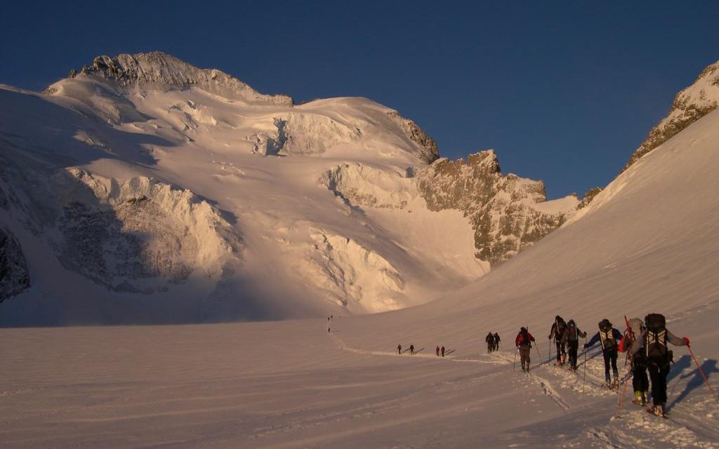 Ski tourers ascending a snowfield toward a peak at dawn